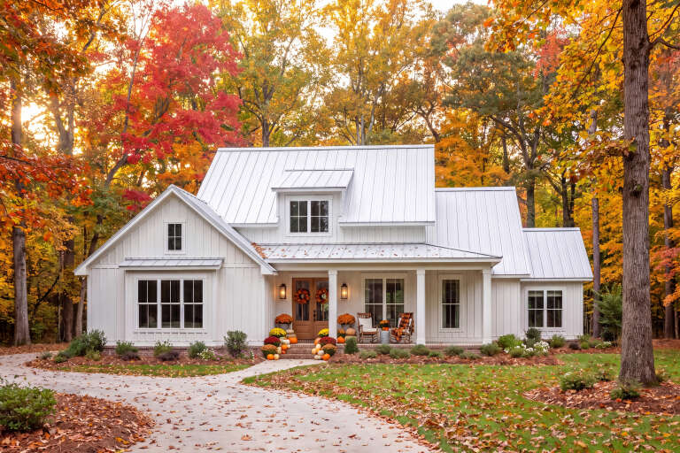 Front view of a white house in Modern Farmhouse style, metal roof, board-and-batten siding, and autumn landscaping. House Plan # 041-00307