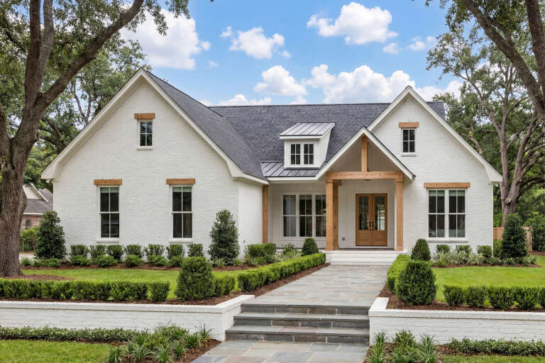 Front view of a white European house, brick siding, wood timber accents, gabled roof, and manicured landscaping. House Plan # 041-00362