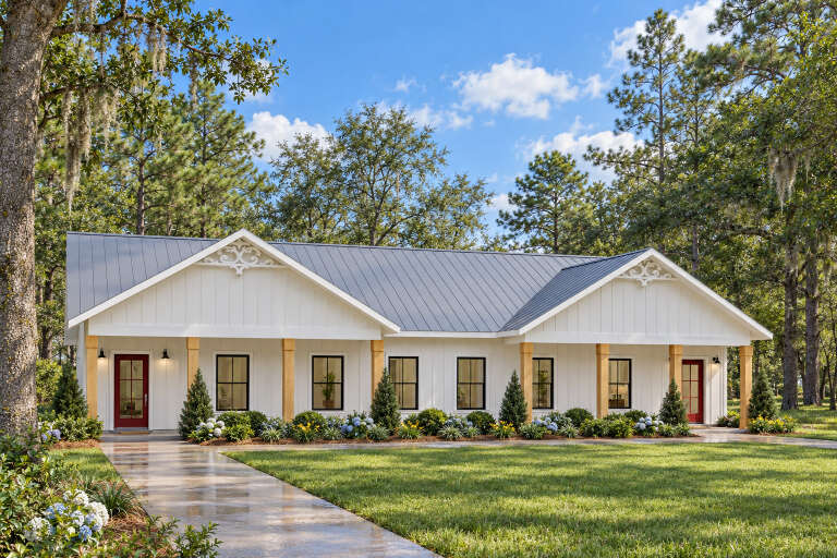 Front view of a white house in Modern Farmhouse style, metal roof, wood columns, red doors, and lush landscaping. House Plan # 1776-00172