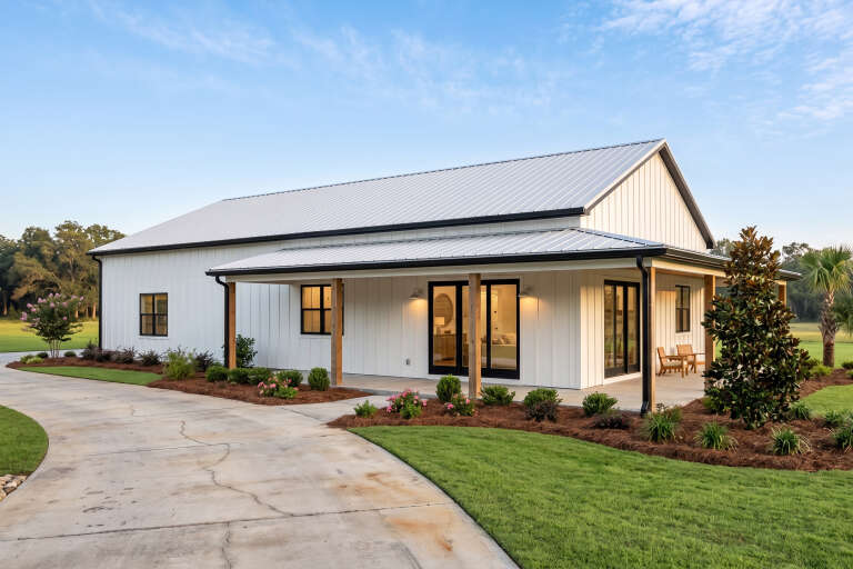 Angled front view of a white house in Barndominium style, metal roof, wood porch posts, black windows, and landscaping. House Plan # 1462-00232