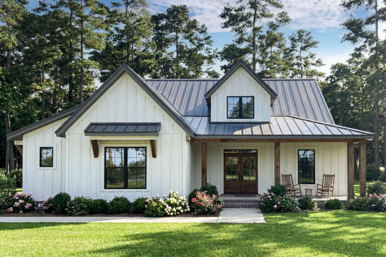 White Modern Farmhouse, Front Elevation, board-and-batten siding, metal roof, wood porch posts, rocking chairs, garden. House Plan # 009-00520 Digital Rendering by America's Best House Plans, Inc.