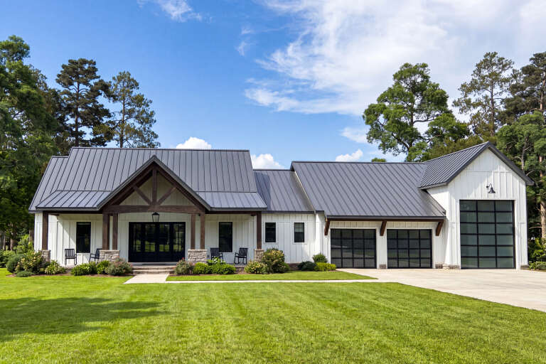 White Barndominium, Front Elevation with metal roof, board-and-batten siding, stone bases, glass garage doors, landscaping. House Plan # 009-00523 Digital Rendering by America's Best House Plans, Inc.