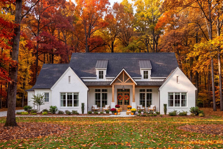 Front view of a white house in Modern Farmhouse style, brick siding, timber porch, dormers, and autumn landscaping. House Plan # 041-00445