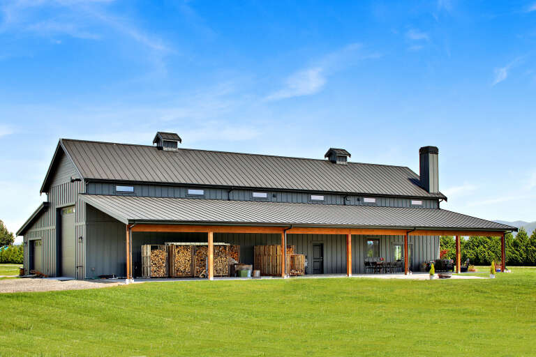 Charcoal Barndominium, Angled Front Elevation, metal siding, wood posts, concrete patio, cupolas, and firewood storage. House Plan # 2464-00247 Digital Rendering by America's Best House Plans, Inc.