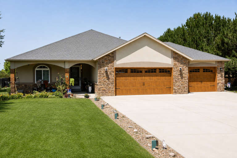 Tan Craftsman, Angled Front Elevation, stone veneer, stucco, arched porch, wood garage doors, concrete drive, landscaping. House Plan # 5244-00028 Digital Rendering by America's Best House Plans, Inc.