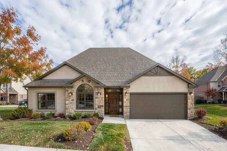 Tan French Country Front Elevation, stucco and stone siding, arched window, wooden door, dark garage, autumn landscaping. House Plan # 4440-00016 Digital Rendering by America's Best House Plans, Inc.