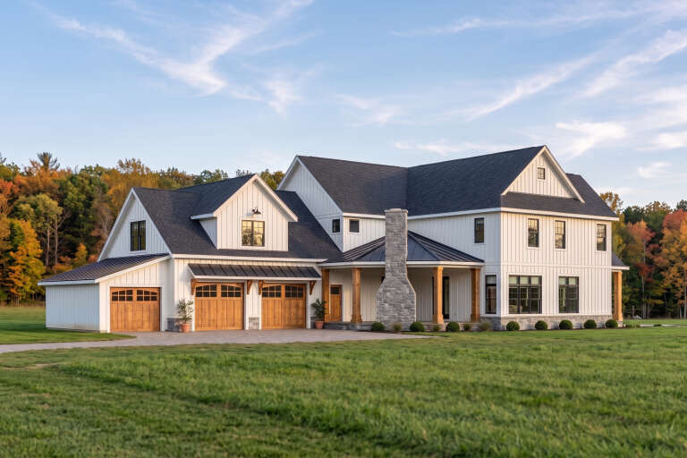 White Modern Farmhouse, Angled Front Elevation with board-and-batten siding, stone chimney, wood garage doors, and lawn. House Plan # 5032-00473 Digital Rendering by America's Best House Plans, Inc.