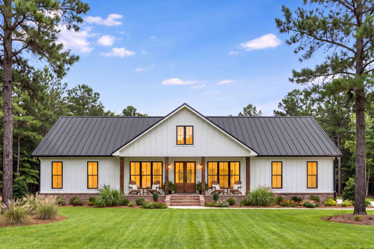 White Modern Farmhouse, Front Elevation, board-and-batten siding, brick base, metal roof, lit porch, wooden door. House Plan # 041-00458 Digital Rendering by America's Best House Plans, Inc.