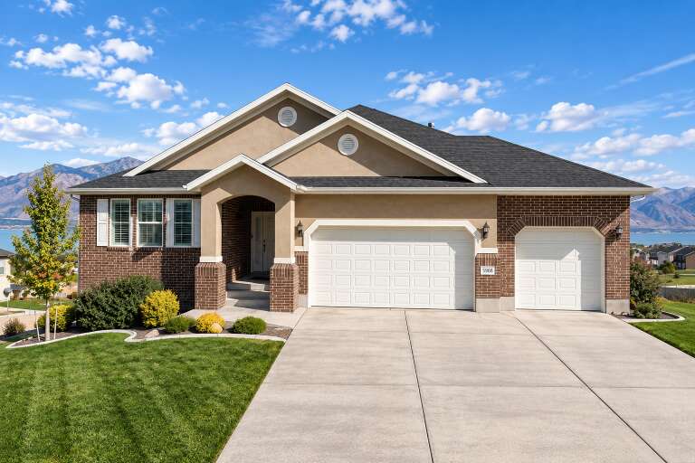 Tan Traditional, Front Elevation with brick and stucco siding, arched garage doors, wall lanterns, and landscaped lawn. House Plan # 2802-00579 Digital Rendering by America's Best House Plans, Inc.