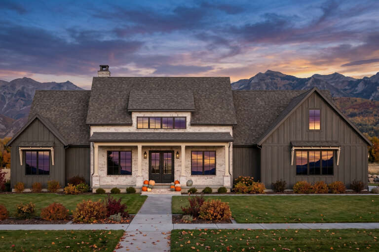 Grey Modern Farmhouse, Front Elevation at dusk, brick and board-batten siding, lit porch, pumpkins, mountain backdrop. House Plan # 7983-00212 Digital Rendering by America's Best House Plans, Inc.