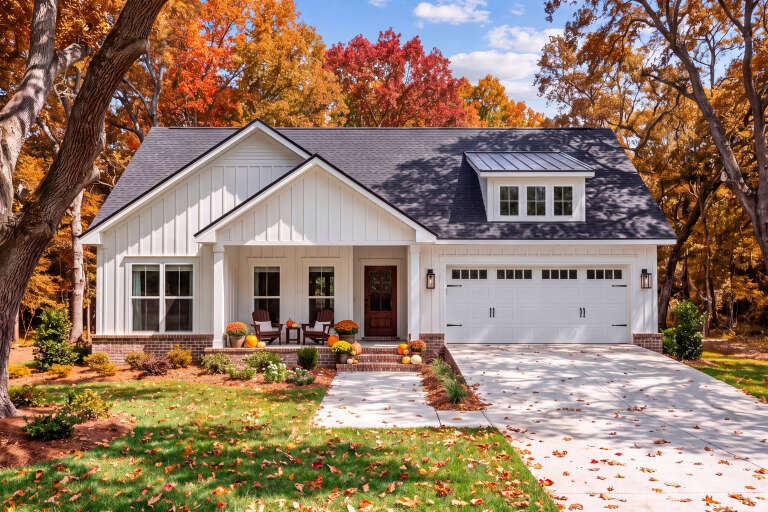 Front view of a white house in Modern Farmhouse style, board-and-batten siding, brick base, porch, and autumn landscape. House Plan # 041-00459