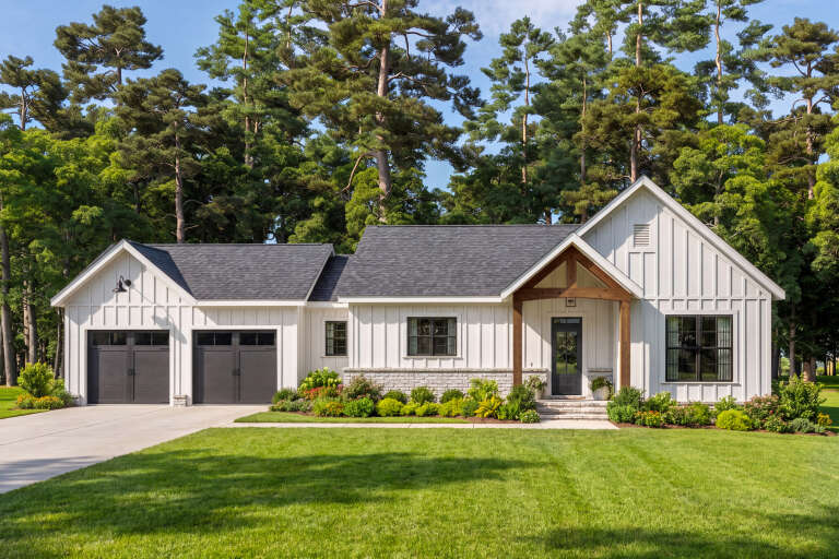 Front view of a white house in Modern Farmhouse style, board-and-batten siding, stone base, wood porch, dark garage. House Plan # 009-00544