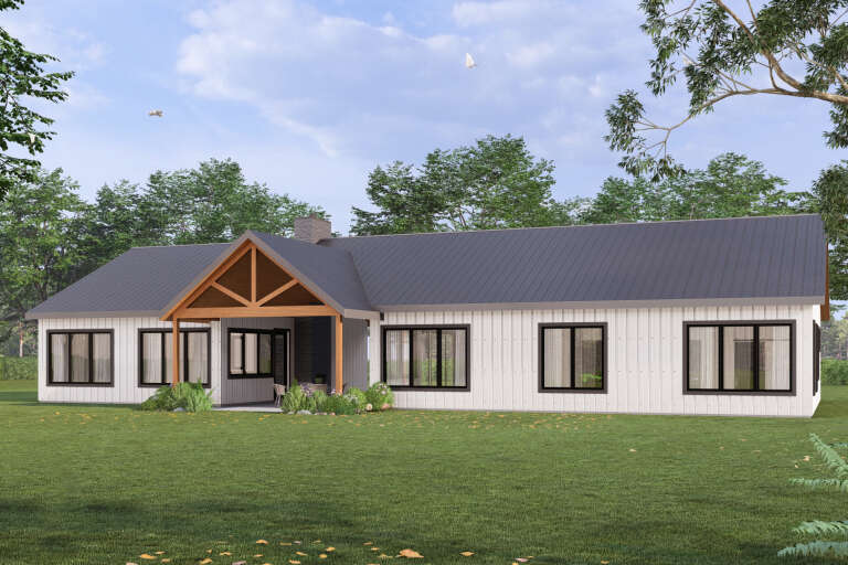 Rear view of a white house, vertical siding, dark metal roof, timber-framed porch, stone chimney, and black windows. House Plan # 3822-00058
