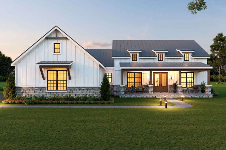 Front view of a white house in Modern Farmhouse style, board-and-batten siding, stone base, metal roof, and front porch. House Plan # 940-01499