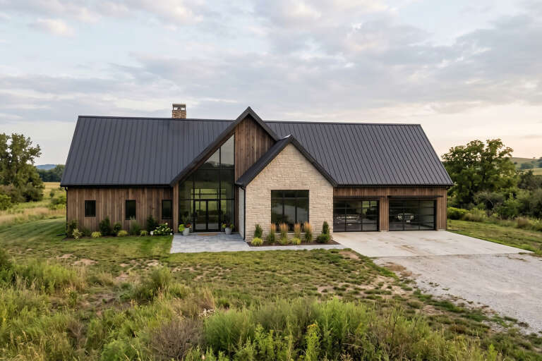 Front view of a brown and stone Barndominium house, metal roof, floor-to-ceiling glass entry, and double garage doors. House Plan # 963-01351