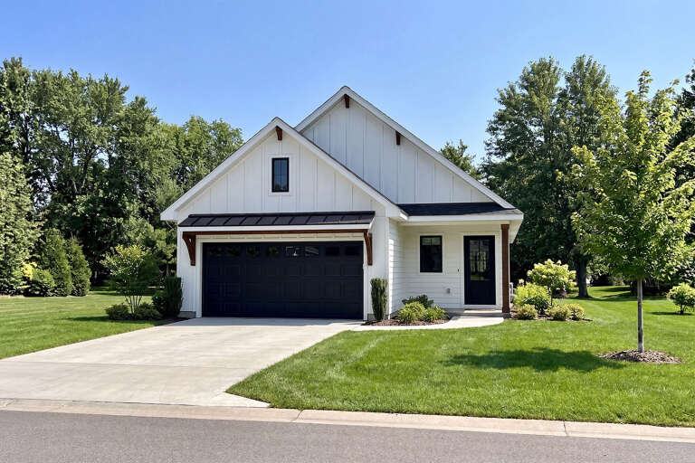 Front view of a white house in Modern Farmhouse style, board-and-batten siding, black garage door, and metal roof accent. House Plan # 402-01939