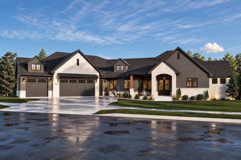 Angled front view of a grey and white stone house, gabled roof, dark garage doors, arched entry, and manicured landscaping. House Plan # 7140-00053