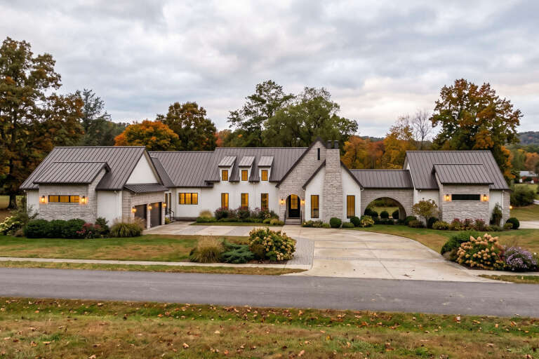 Front view of a white and stone Modern Transitional house, metal roof, arched breezeway, and landscaped driveway. House Plan # 963-01354